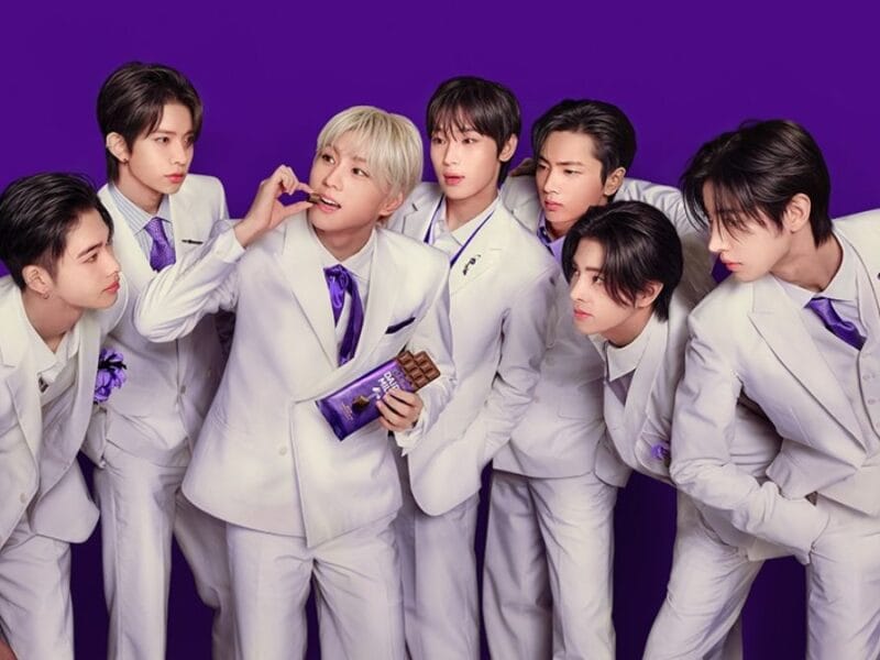 An ENHYPEN member eats Cadbury while his bandmates look on